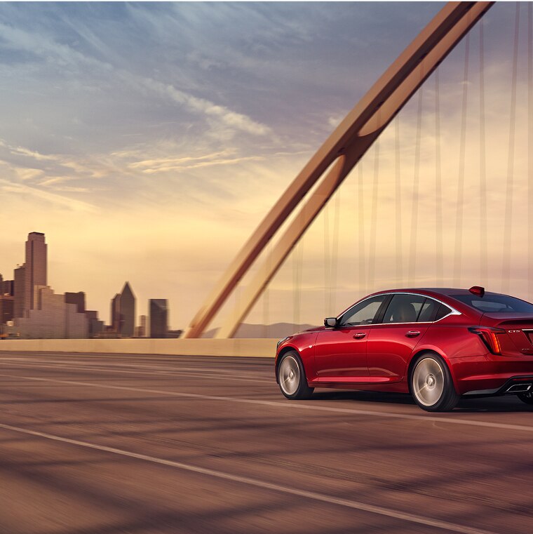 A Red Cadillac CT5 Driving on a Bridge Towards a City Landscape