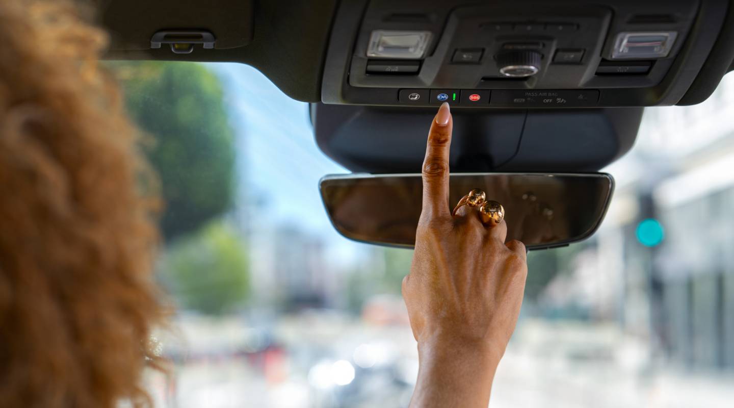 Close-up of a Woman Pressing the OnStar Button on a Vehicle’s Roof Controls