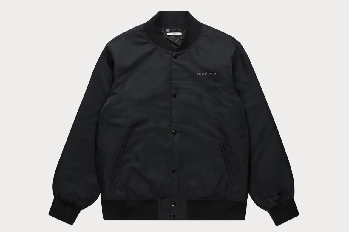 Black Collegiate Bomber Jacket With General Motors Text on Chest. It Has Button-Up Front, Side Pickets, and Ribbed Cuffs