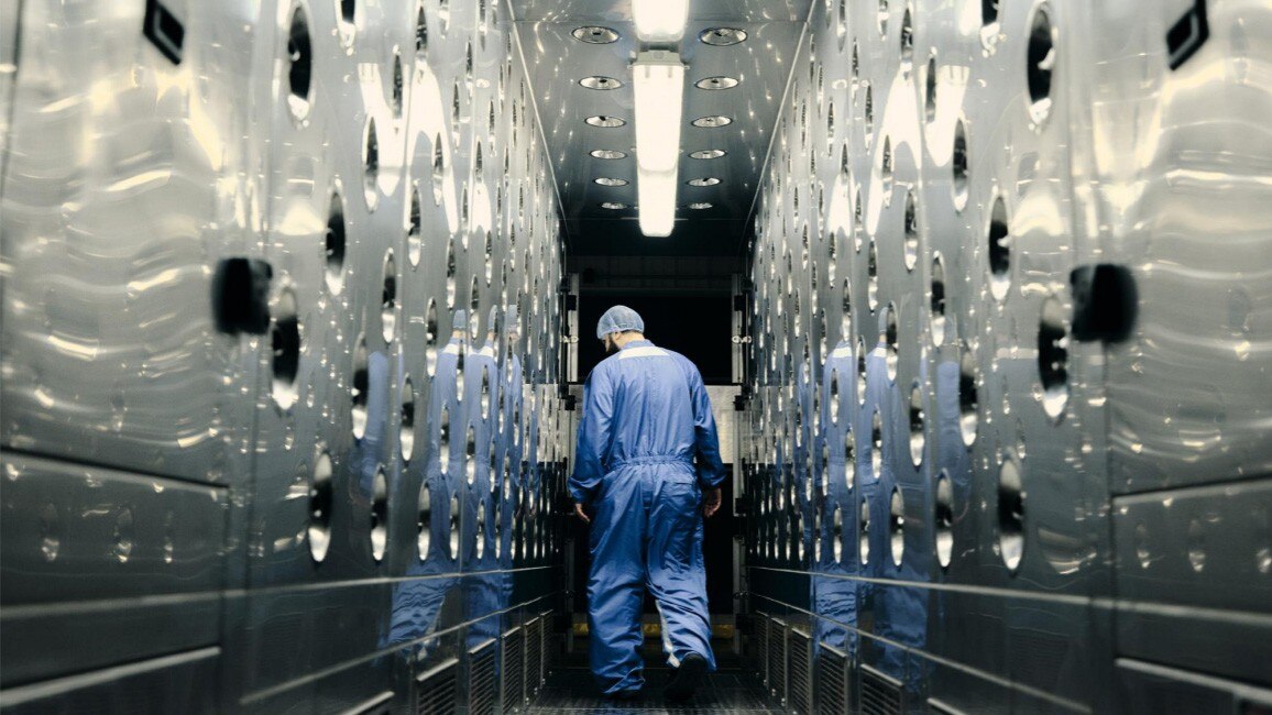 A GM Technician in a Full-body Suit and Hairnet in a Brightly Lit Lab Lined with Circular Indentations on Both Sides