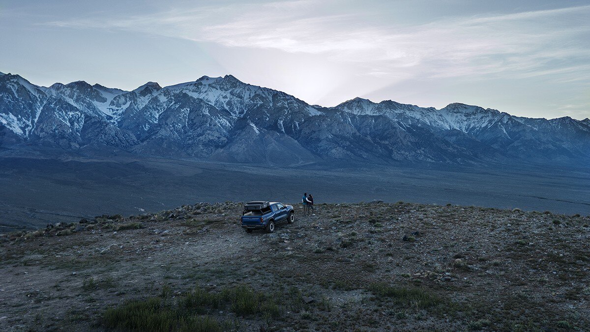 Bird's Eye View of a Couple Outlooking a Beautiful Mountain Landscape Standing Next to an Off-roading GM Vehicle