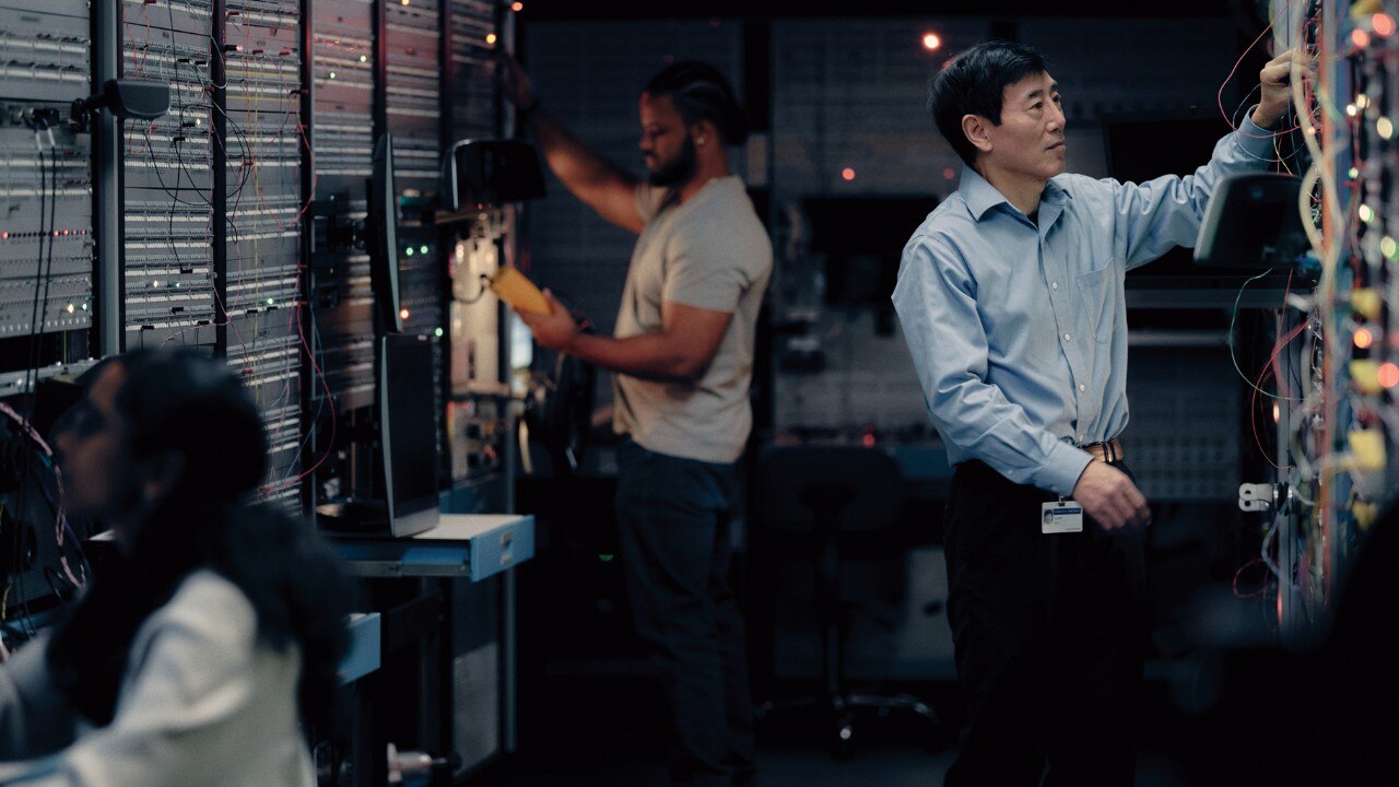 Two Men and a Woman Plugging in Wires in a Behind-the-scenes Data Center