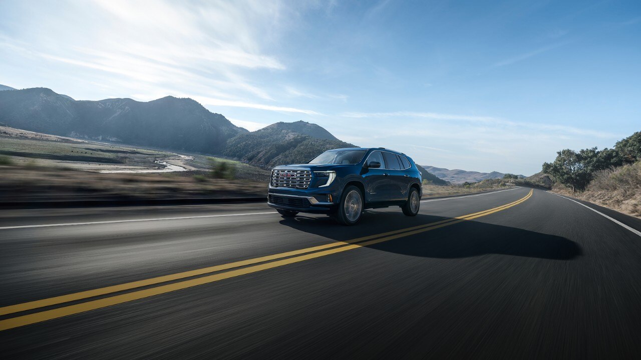 Wide Three-quarters View of a GMC Vehicle Driving Down a Road in the Mountains